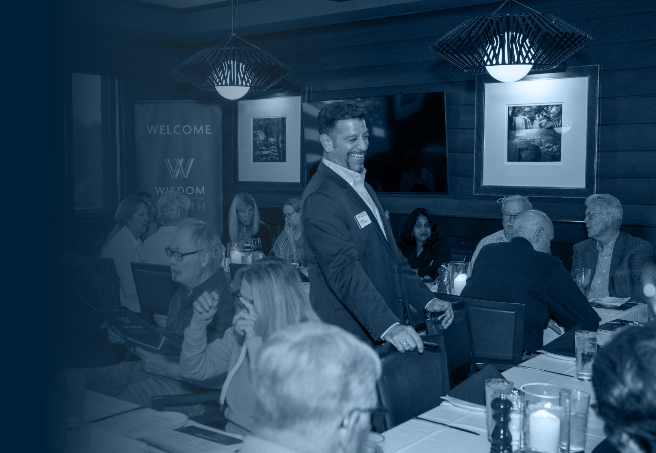A smiling man standing at a dinner event- Wisdom to Wealth